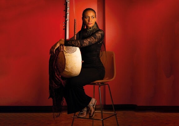 Sona Jobarteh seated against red background holding instrument
